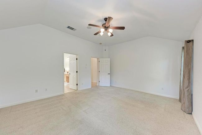Unfurnished bedroom with baseboards, light carpet, connected bathroom, visible vents, and lofted ceiling | Image 23