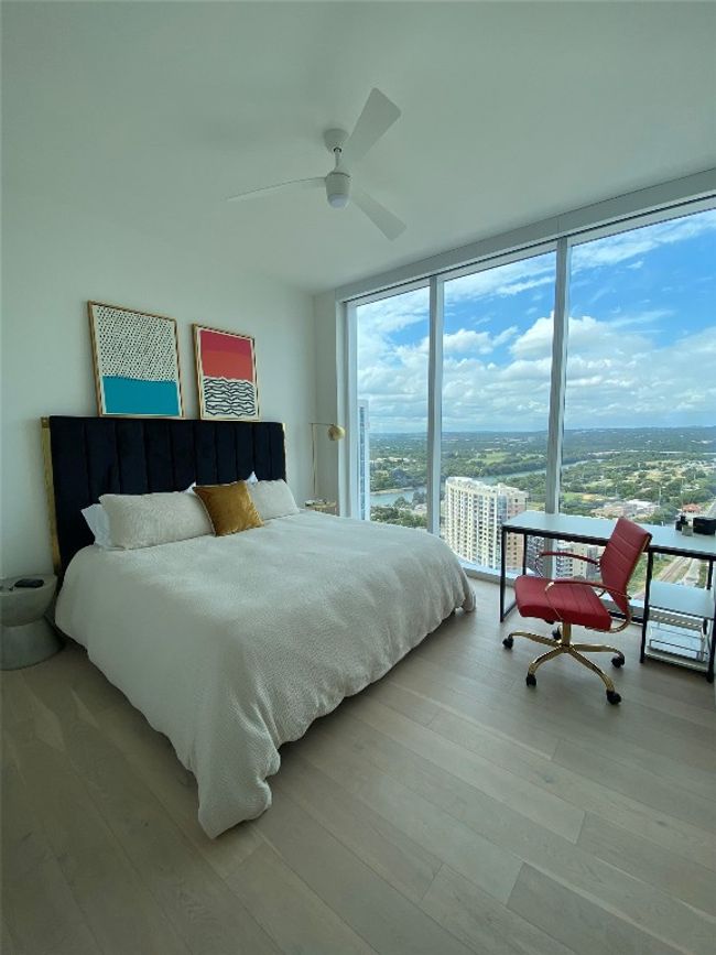 Bedroom with multiple windows, wood finished floors, a ceiling fan, expansive windows, and a city view | Image 8