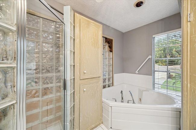 Upstairs ensuite bathroom features a glass block shower, a corner jetted tub, and a large window offering natural light. The space includes textured cabinets for storage and a neutral color scheme. | Image 26