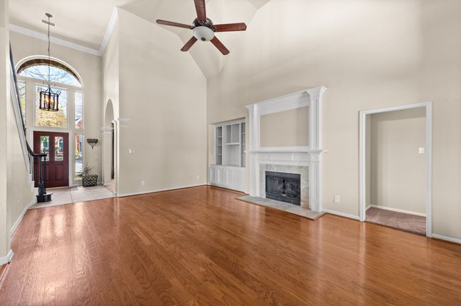 Unfurnished living room with a towering ceiling, a chandelier, a tiled fireplace, ceiling fan, and wood finished floors | Image 13