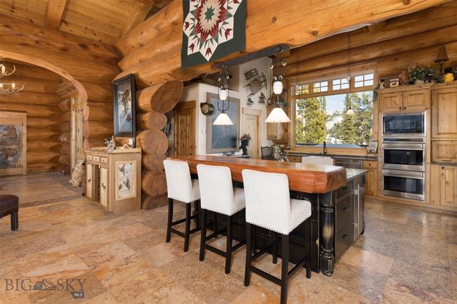 Main level kitchen with pendant lighting, island with wooden slab counter, side custom made bar area and stainless steel appliances. | Image 30