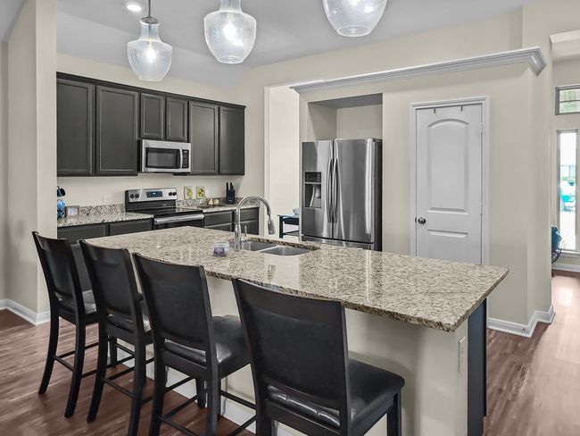 Kitchen with stainless steel appliances, dark wood-style flooring, a breakfast bar area, and light stone counters | Image 6