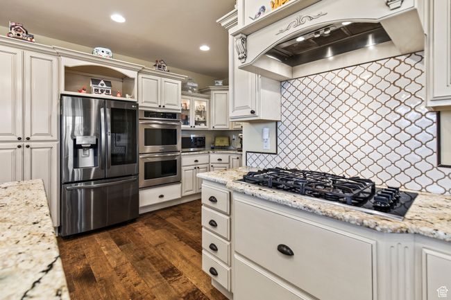 Kitchen with light stone countertops, dark wood-type flooring, stainless steel appliances, range hood, and white cabinets | Image 30