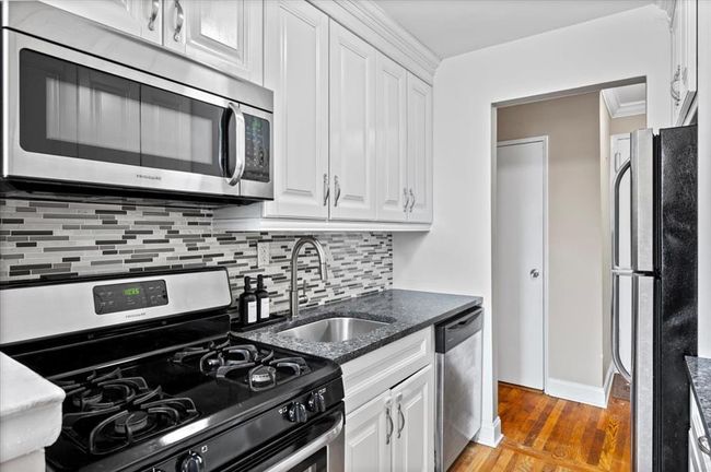 Kitchen featuring stainless steel appliances, white cabinetry, tasteful backsplash, light wood-style floors, and dark stone counters | Image 13