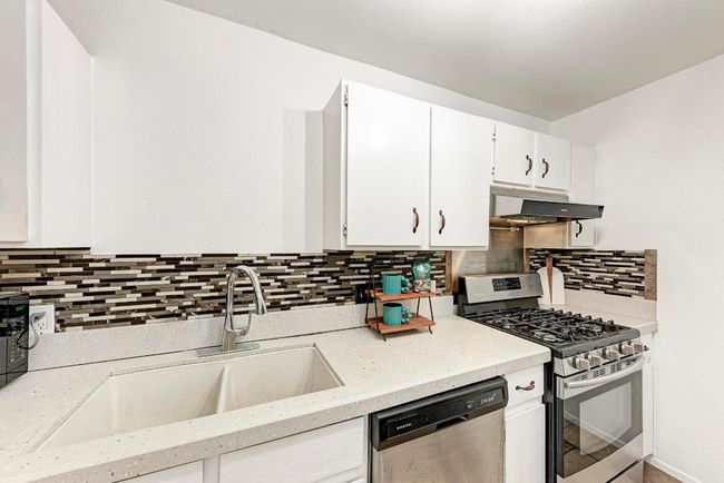 Kitchen with under cabinet range hood, appliances with stainless steel finishes, white cabinets, and a sink | Image 15