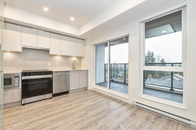 Kitchen with stainless steel appliances, a baseboard radiator, light wood finished floors, light countertops, and white cabinetry | Image 5