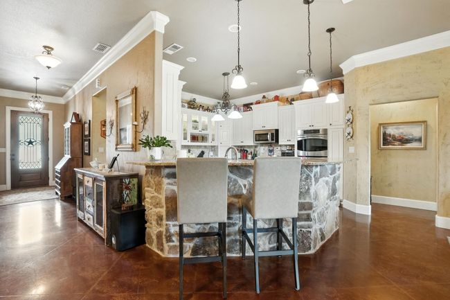 Kitchen with crown molding, glass insert cabinets, a breakfast bar area, white cabinets, and appliances with stainless steel finishes | Image 9