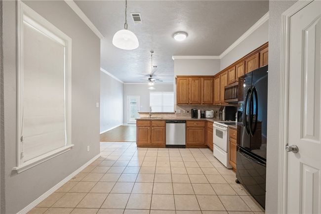 Kitchen featuring appliances with stainless steel finishes, ornamental molding, brown cabinets, light tile patterned flooring, and ceiling fan | Image 4