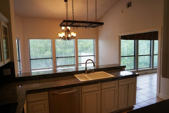 Kitchen with stainless steel dishwasher, a sink, a chandelier, vaulted ceiling, and light tile patterned flooring | Image 11