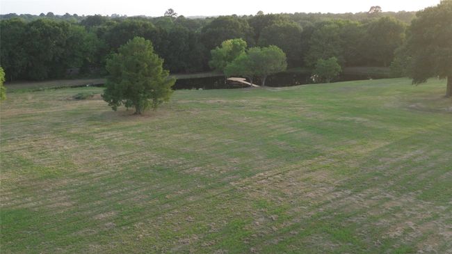 Expansive, gently sloping grassy land with a serene pond surrounded by lush trees, offering a peaceful, natural setting perfect for a private retreat or home build. | Image 49