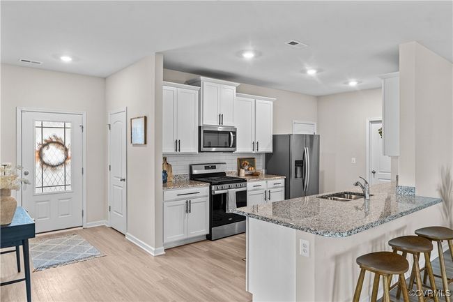 Kitchen with stainless steel appliances, a sink, a breakfast bar area, light wood finished floors, and decorative backsplash | Image 16