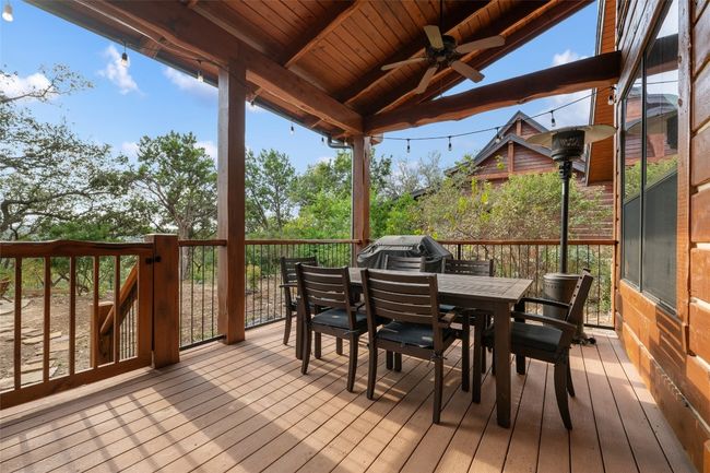 This spacious back deck offers a perfect spot for outdoor dining and relaxation, complete with a ceiling fan and string lights for evening ambiance. Surrounded by trees and natural views, it's ideal for gathering with friends or enjoying a quiet meal in a serene setting. | Image 19