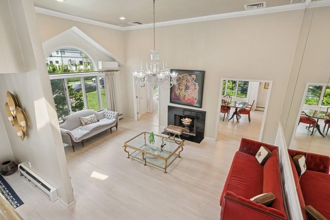 Living area with baseboard heating, healthy amount of natural light, a high ceiling, a chandelier, and a wall unit AC | Image 4