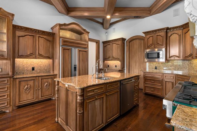 Kitchen featuring built in appliances, decorative backsplash, a kitchen island with sink, coffered ceiling, and dark wood-type flooring | Image 19
