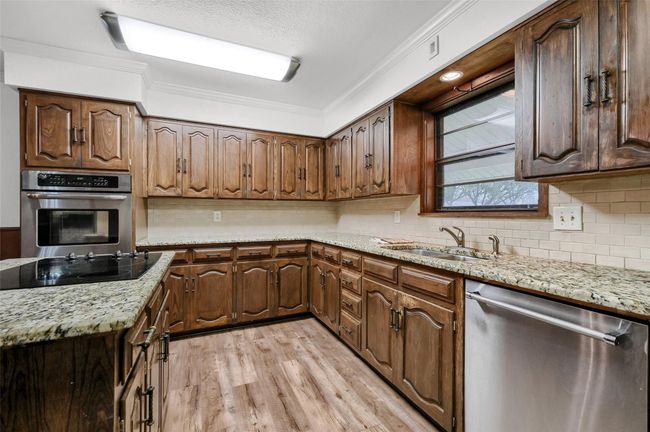 Kitchen featuring appliances with stainless steel finishes, crown molding, a sink, light wood finished floors, and decorative backsplash | Image 8