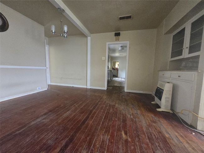 Unfurnished living room with dark wood finished floors, a glass covered fireplace, heating unit, a chandelier, and baseboards | Image 4