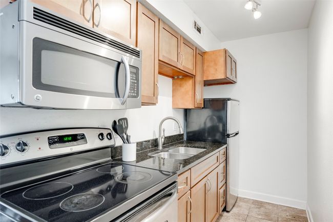 Kitchen featuring stainless steel appliances, a sink, baseboards, dark stone countertops, and light tile patterned flooring | Image 12