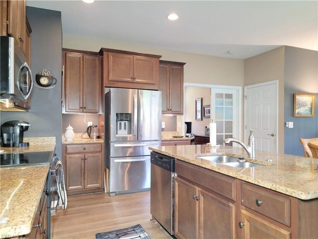 Kitchen with a sink, light wood-style floors, a kitchen island with sink, stainless steel appliances, and light stone countertops | Image 11