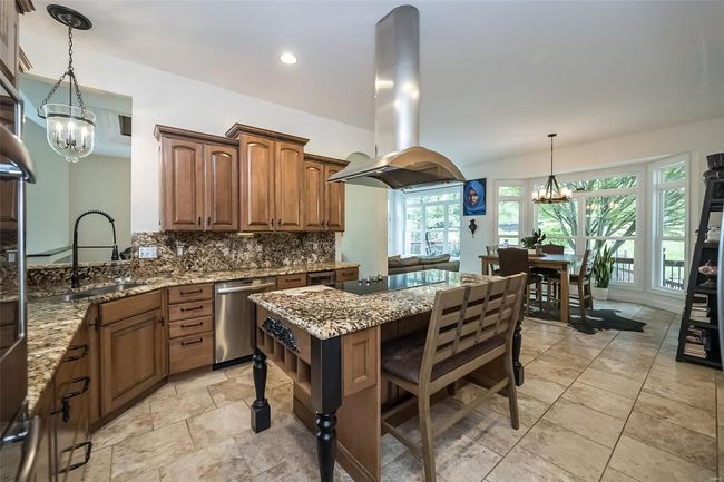 Kitchen featuring light stone counters, a sink, dishwasher, a chandelier, and island range hood | Image 19