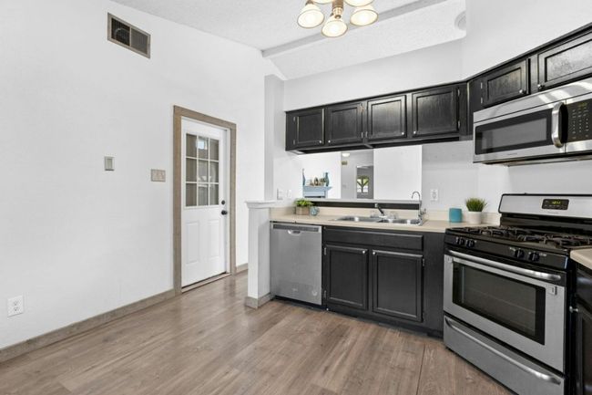 Kitchen featuring appliances with stainless steel finishes, dark cabinetry, lofted ceiling, light wood finished floors, and light countertops | Image 12