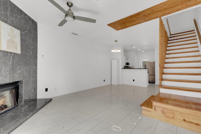 Unfurnished living room with light marble finish flooring, a fireplace, stairway, and a ceiling fan | Image 6