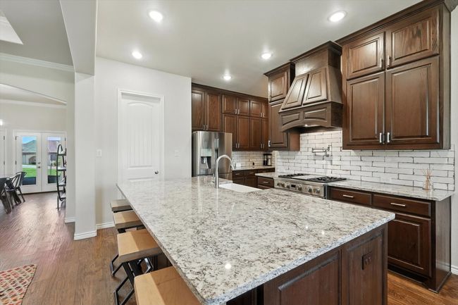 Kitchen featuring stainless steel fridge with ice dispenser, custom range hood, tasteful backsplash, crown molding, and light stone countertops | Image 14