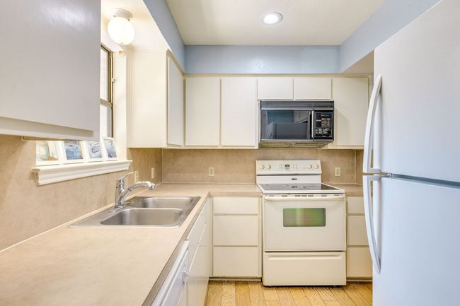 Kitchen featuring white appliances, a sink, light countertops, light wood finished floors, and recessed lighting | Image 7