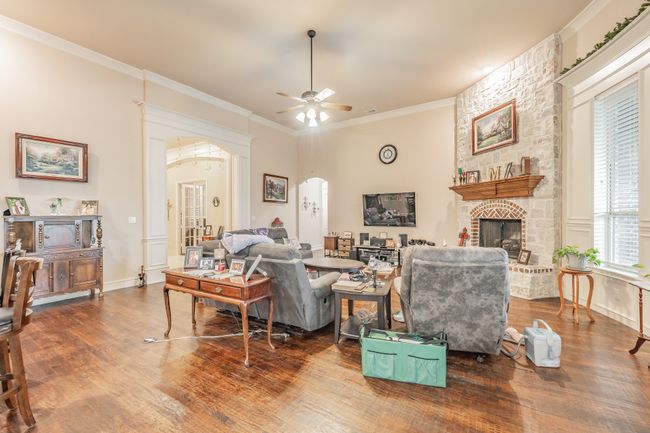 Living room with arched walkways, wood finished floors, ceiling fan, a fireplace, and ornamental molding | Image 12