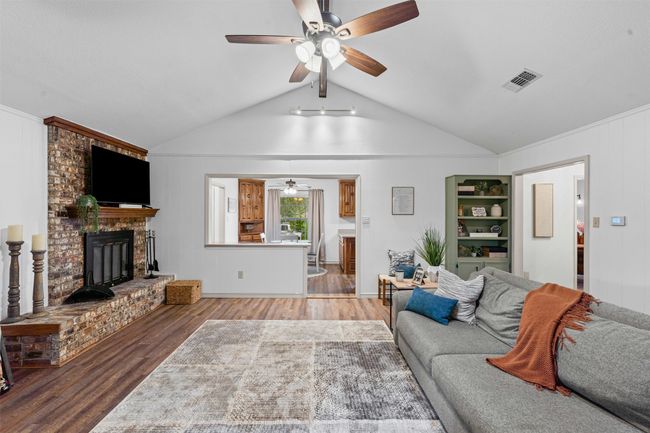 Living room featuring a ceiling fan, wood finished floors, a fireplace, and lofted ceiling | Image 8