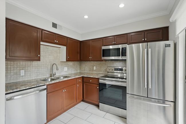 Kitchen featuring appliances with stainless steel finishes, a sink, light tile patterned flooring, light stone countertops, and ornamental molding | Image 14