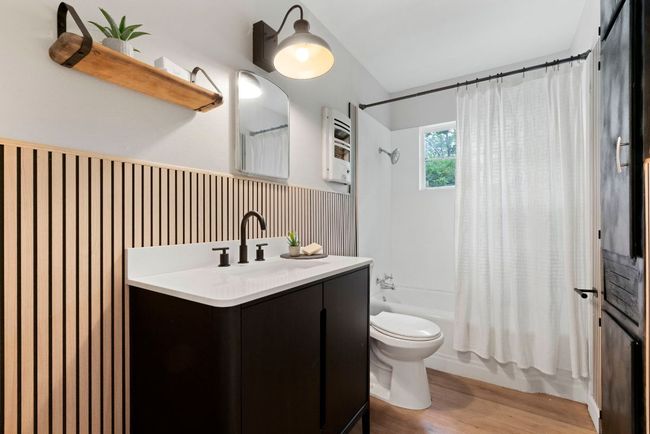 The full bathroom is well crafted and features a sophisticated light fixture, laminate flooring, and a bathtub/shower combo brightened by a window. | Image 16