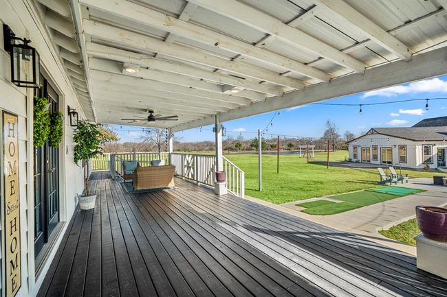 The deep covered porch spans the front of the home—offering shaded outdoor living space with views across the 7-acre property. | Image 25