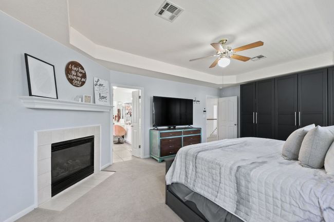 Bedroom with light colored carpet, a tile fireplace, ensuite bath, a tray ceiling, and ceiling fan | Image 18