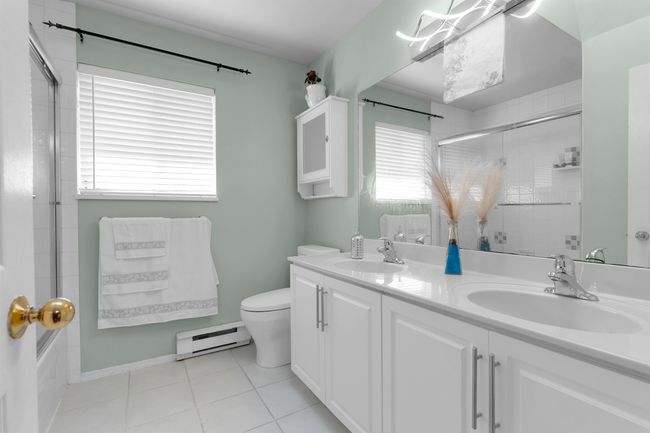 Full bath with a shower with shower door, a baseboard heating unit, double vanity, tile patterned flooring, and a tub | Image 11