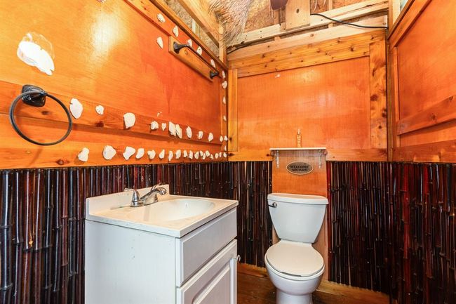 This ground floor half bath features a rustic design with wood paneling and unique decorative accents. It includes a white sink with storage and a toilet, creating a cozy, cabin-like atmosphere. | Image 44