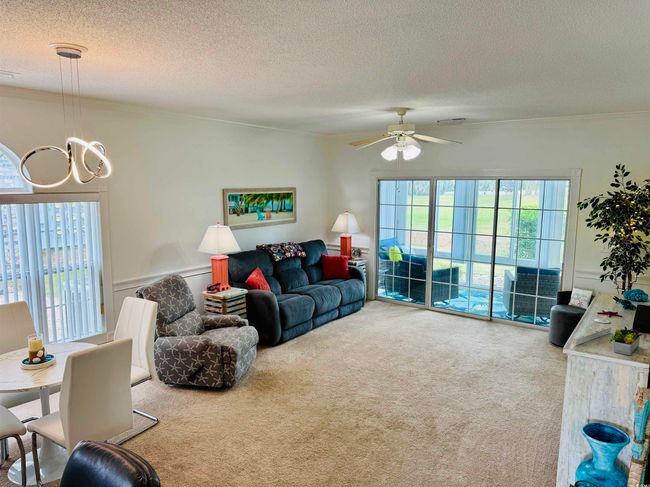 Carpeted living area with crown molding, a chandelier, a ceiling fan, a textured ceiling, and a wainscoted wall | Image 21