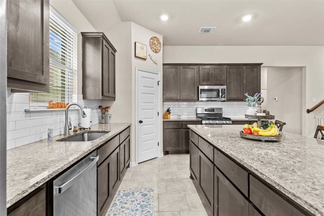 Kitchen with stainless steel appliances, decorative backsplash, dark brown cabinets, light stone countertops, and recessed lighting | Image 7