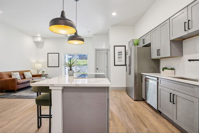 Kitchen featuring gray cabinetry, hanging light fixtures, a kitchen island, a breakfast bar area, and light stone counters | Image 7