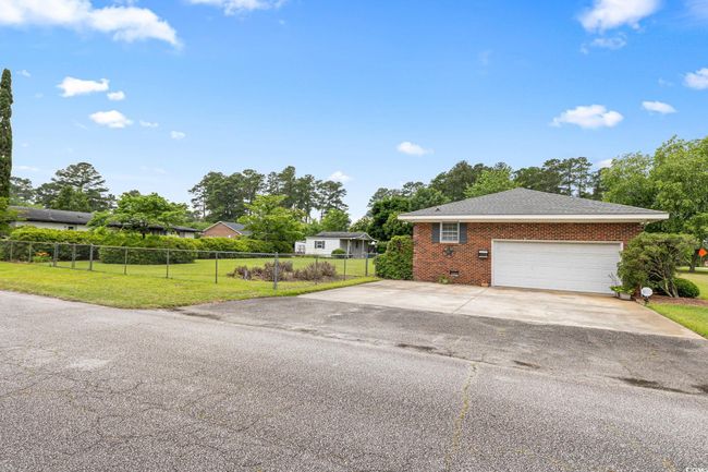 View of side of property with concrete driveway, brick siding, roof with shingles, and an attached garage | Image 6