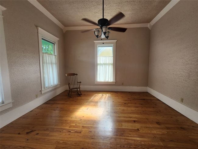 Unfurnished room featuring a textured ceiling, plenty of natural light, a textured wall, wood finished floors, and crown molding | Image 15