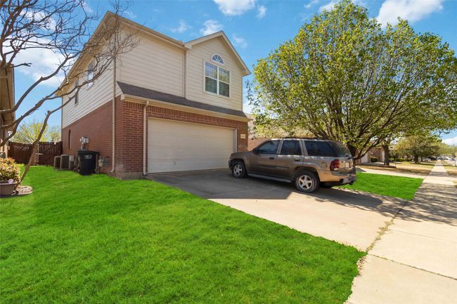 View of home's exterior with driveway, an attached garage, a yard, central air condition unit, and brick siding | Image 4