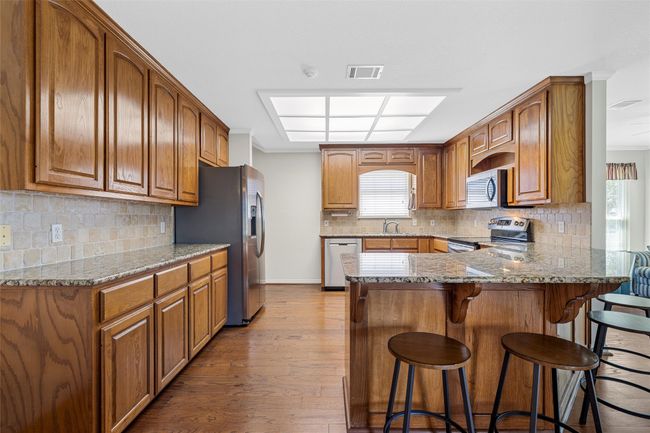 Kitchen featuring brown cabinets, stainless steel appliances, wood finished floors, visible vents, and a peninsula | Image 9