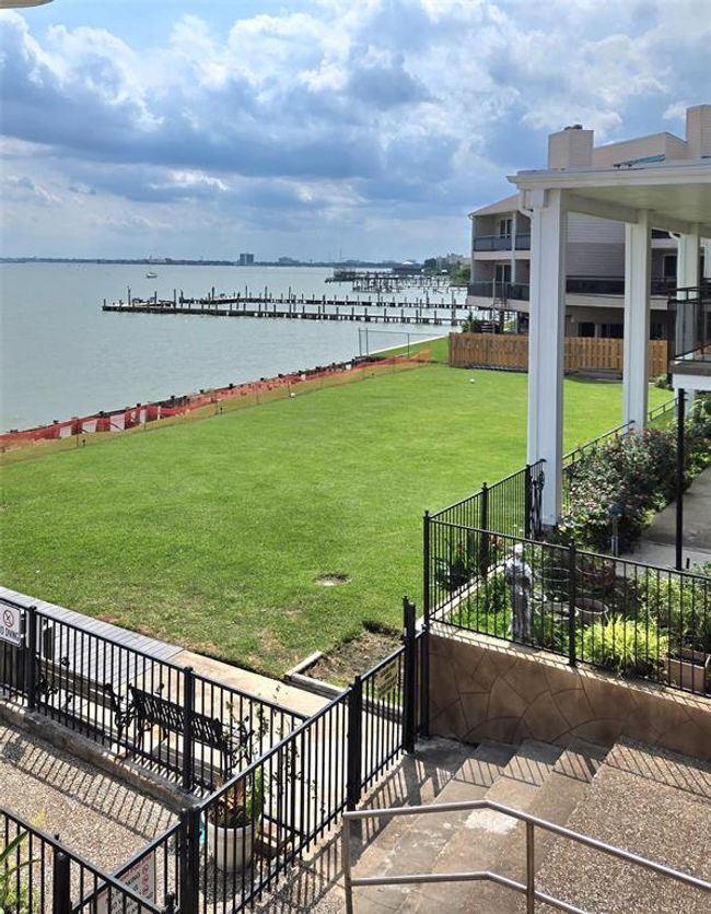 This photo showcases a waterfront property with a spacious lawn leading to a scenic view of the water. There's a nearby dock, and the area is fenced with a mix of greenery and open space, offering a serene and picturesque setting. | Image 23