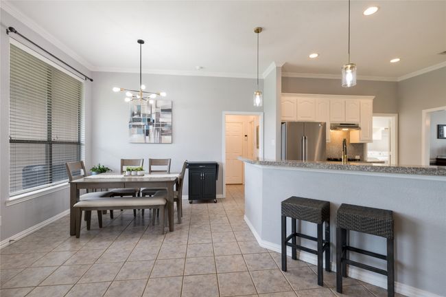 Kitchen featuring freestanding refrigerator, crown molding, white cabinets, a breakfast bar, and a chandelier | Image 18
