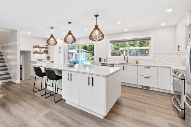 Kitchen featuring a center island, white cabinets, a sink, light countertops, and light wood finished floors | Image 11