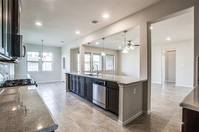 Modern kitchen with granite countertops, stainless steel appliances, and tiled flooring extending into a spacious, well-lit breakfast area | Image 6