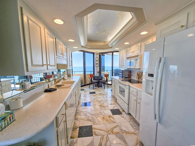 Kitchen featuring a sink, white appliances, light countertops, marble finish floor, and a tray ceiling | Image 11
