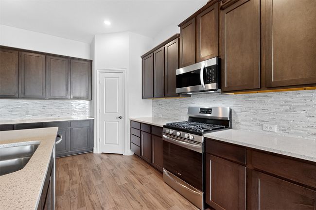 Kitchen with appliances with stainless steel finishes, dark brown cabinets, backsplash, light stone counters, and light wood-type flooring | Image 8