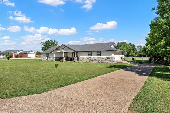 Ranch-style house featuring driveway, stone siding, a front yard, and covered porch | Image 25