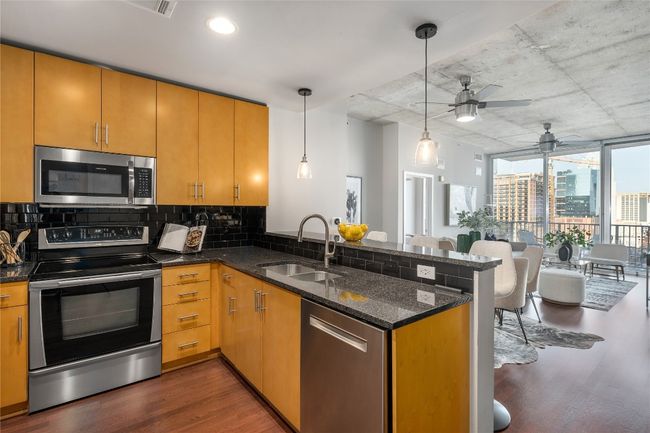 Kitchen featuring stainless steel appliances, a peninsula, dark wood-style flooring, decorative backsplash, and ceiling fan | Image 7